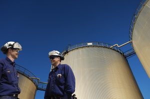oil and gas workers in front of large fuel storage tanks